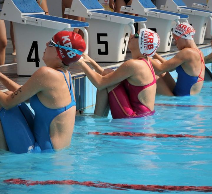 Swimmers standing on starting blocks at an outdoor competition pool